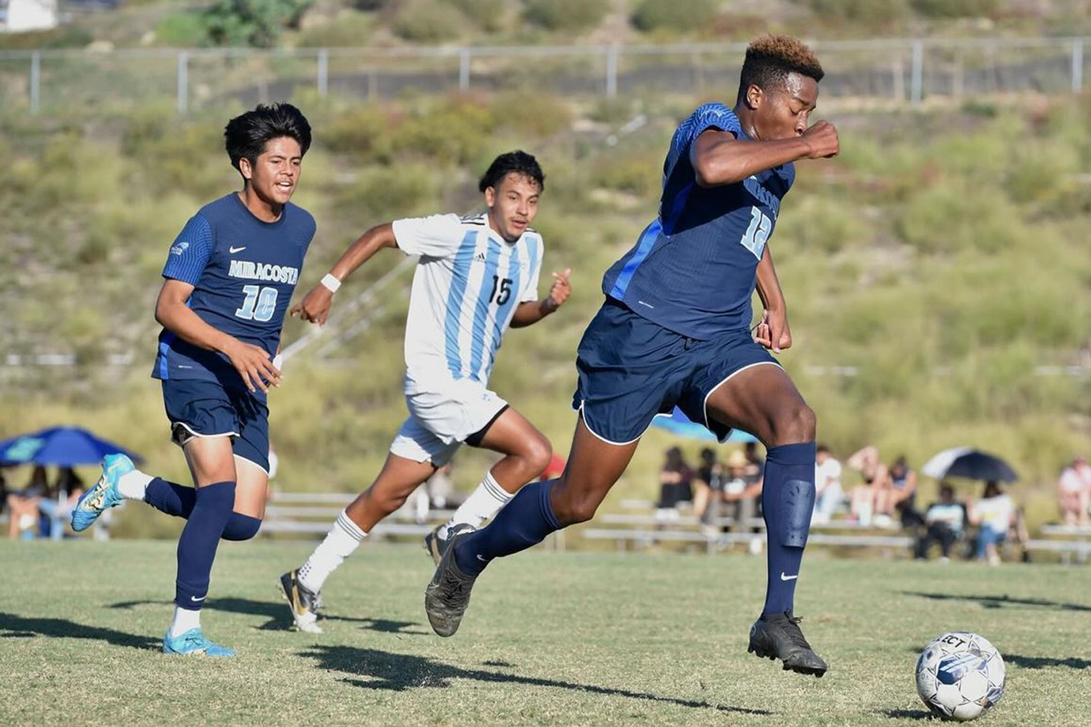 Men's Soccer player, Luke Adomey, dribbles the soccer ball as teammate Alexis Aparicio runs behind him.